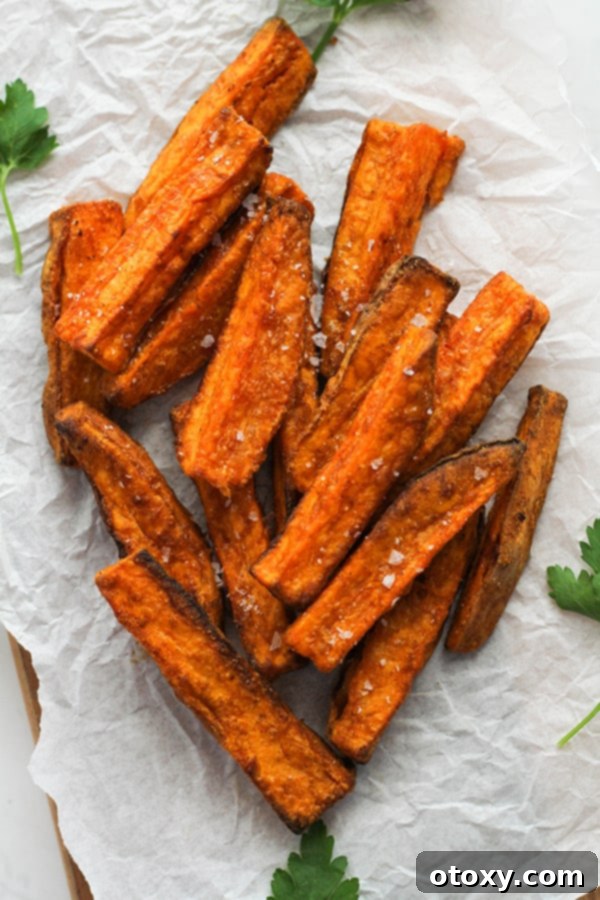Freshly air-fried sweet potato wedges on white parchment paper, lightly salted.