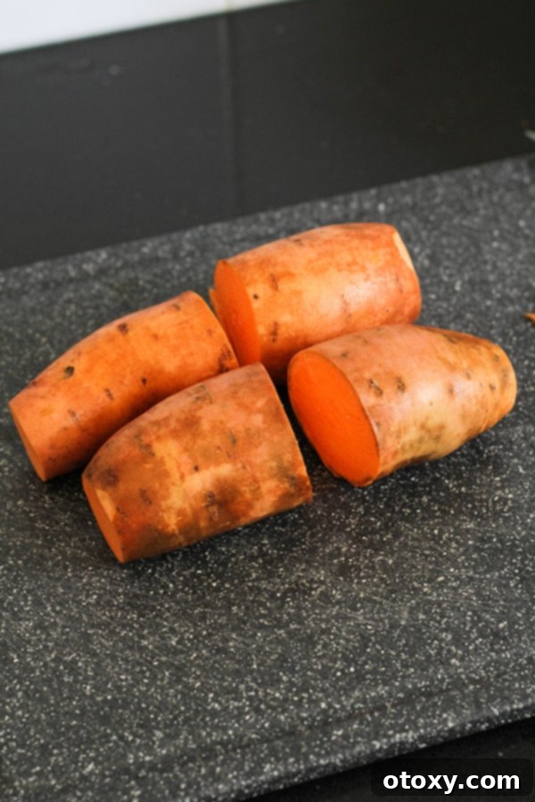A large sweet potato cut in half horizontally on a wooden cutting board, ready for slicing.