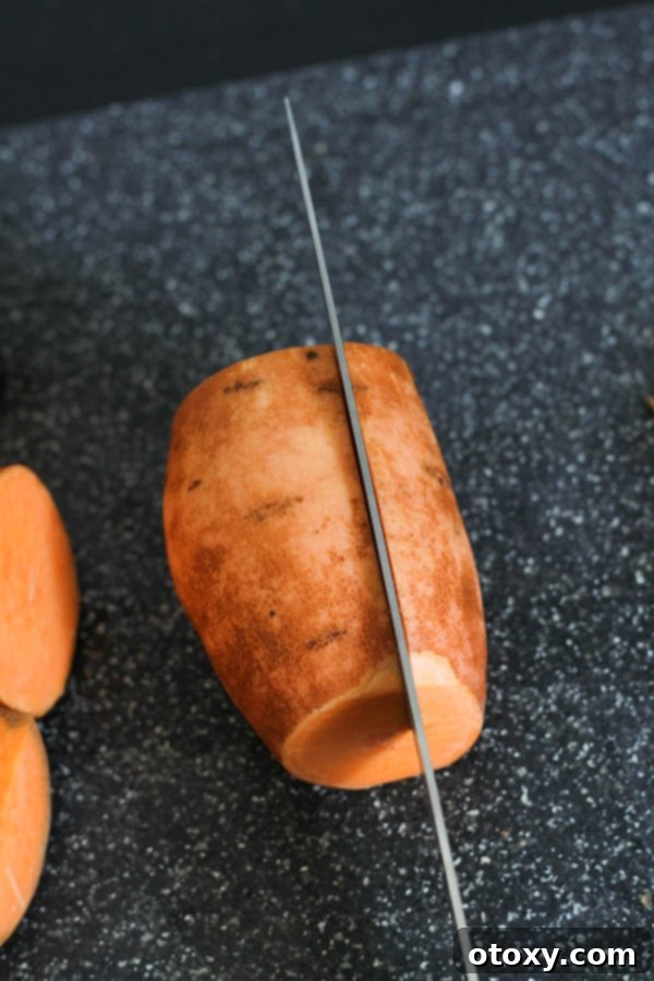 A knife slicing a sweet potato half into three thick, even sections lengthwise.