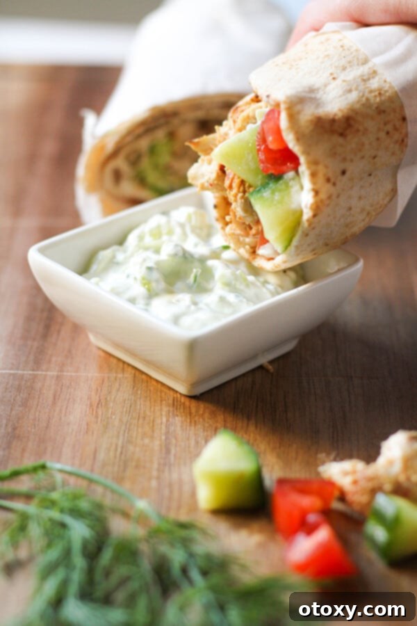 Hand dipping a chicken gyro wrap into a bowl of creamy tzatziki sauce.