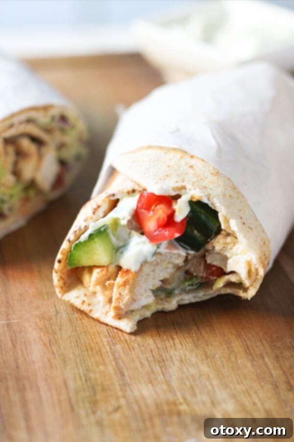 A freshly made chicken gyro with a bite removed, showcasing its delicious layers of chicken, tzatziki, and salad, served on a rustic wooden board.