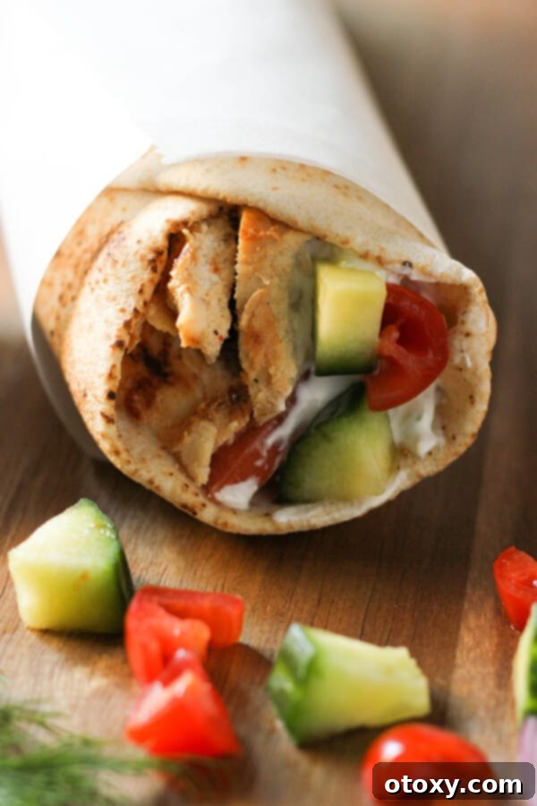 A close-up of a chicken gyro neatly wrapped in parchment paper, showcasing the appealing presentation and vibrant fillings.