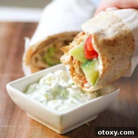 Hand dipping a chicken gyro into a bowl of tzatziki sauce