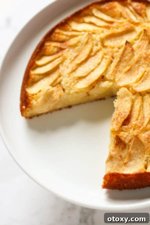 apple cake with a slice missing on a white cake stand.