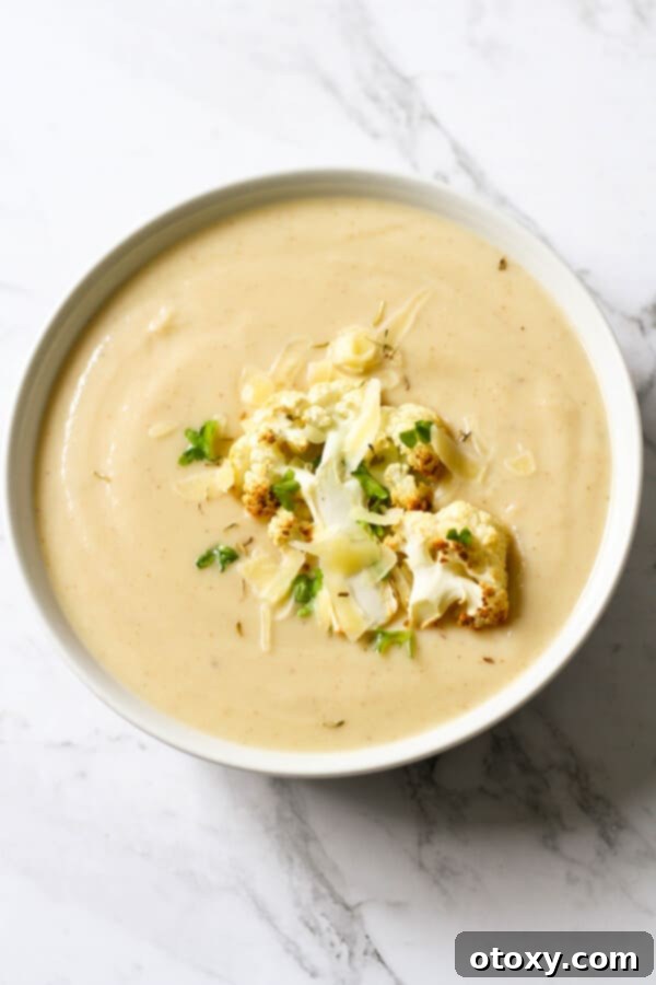 a bowl of cauliflower soup with roasted cauliflower, shredded cheese and parsley on top.