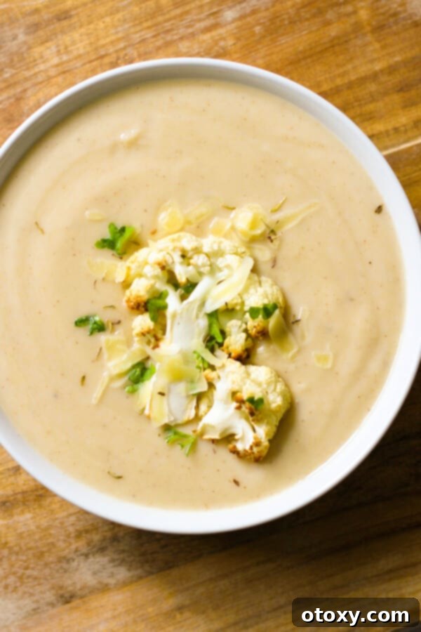 a bowl of cauliflower soup with roasted cauliflower, shredded cheese and parsley on top.