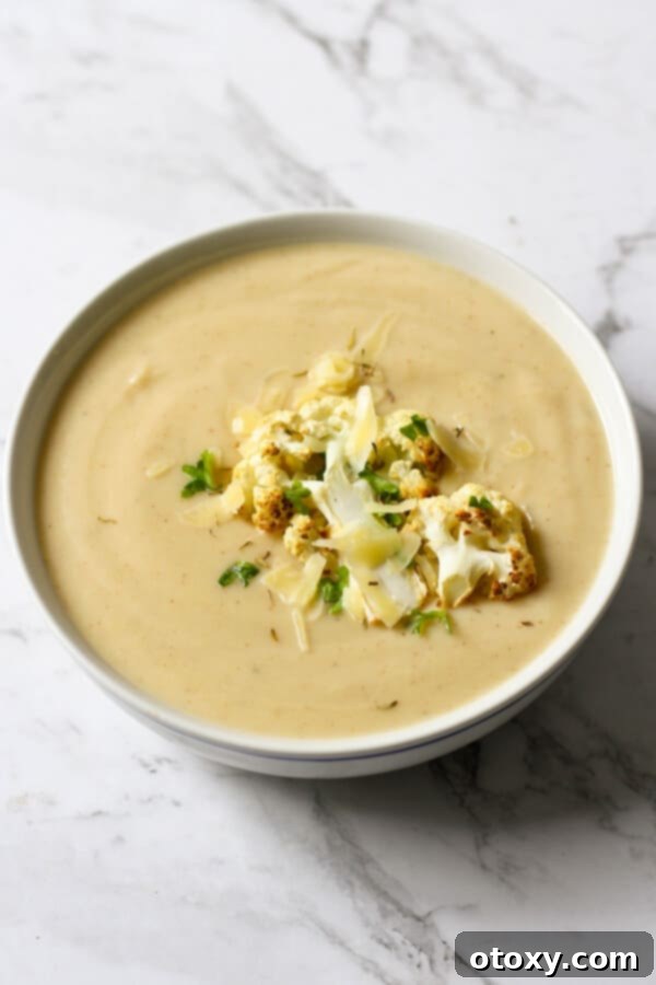 a bowl of cauliflower soup with roasted cauliflower, shredded cheese and parsley on top.