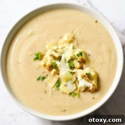 a bowl of cauliflower soup with roasted cauliflower, shredded cheese and parsley on top.