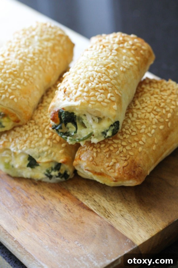 Spinach Ricotta Rolls Oven or Air Fried 12 A stack of golden brown spinach and ricotta rolls on a wooden board, highlighting their flaky pastry and appealing presentation.