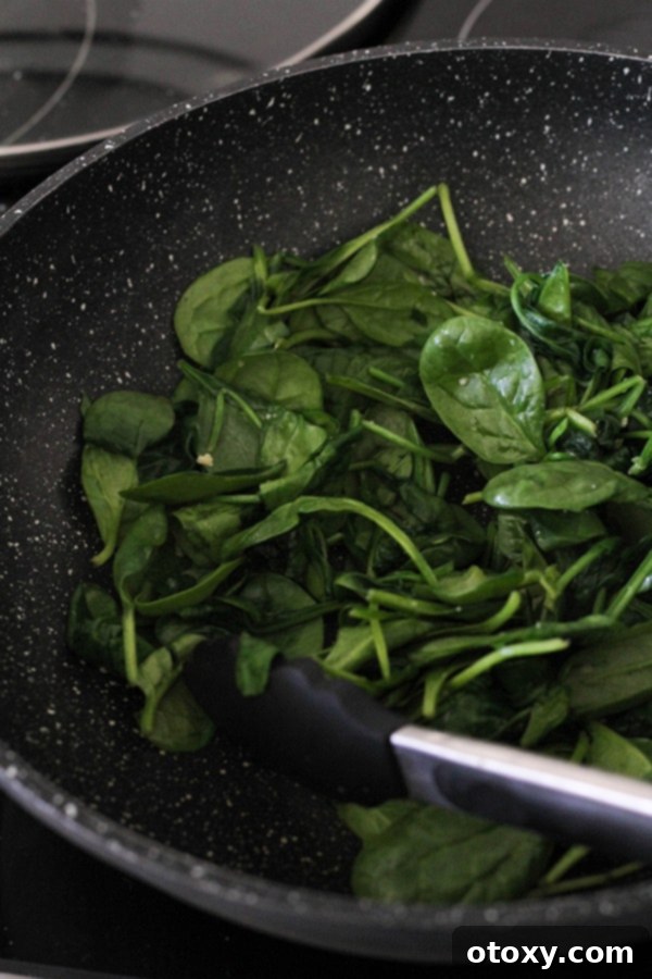 Spinach Ricotta Rolls Oven or Air Fried 5 Fresh baby spinach wilting in a hot wok with garlic, a crucial step for the spinach and ricotta roll filling.