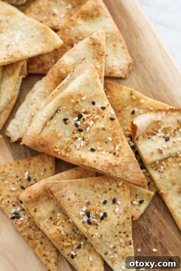 pita chips on a wooden board. A rustic wooden board holds a generous pile of golden-brown, triangular pita chips, perfectly baked and ready for dipping.