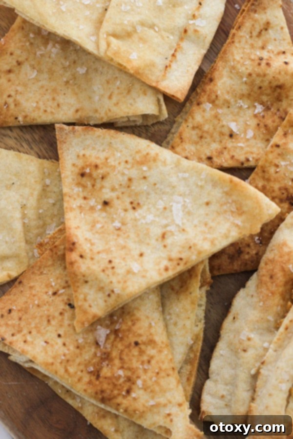 baked pita chips stacked on top of each other. A neat stack of perfectly golden and crispy homemade pita chips sits on a wooden surface, highlighting their inviting texture.