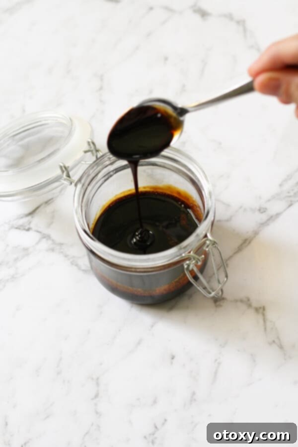 A glass jar filled with homemade balsamic glaze, with a spoon resting just above it, ready to drizzle.
