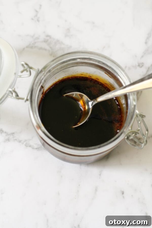 An open glass jar filled with luscious balsamic glaze, a spoon resting inside, ready for use.