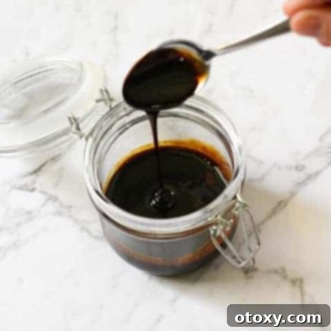 A glass jar of homemade balsamic glaze with a spoon, ready to be drizzled over your favorite dishes.