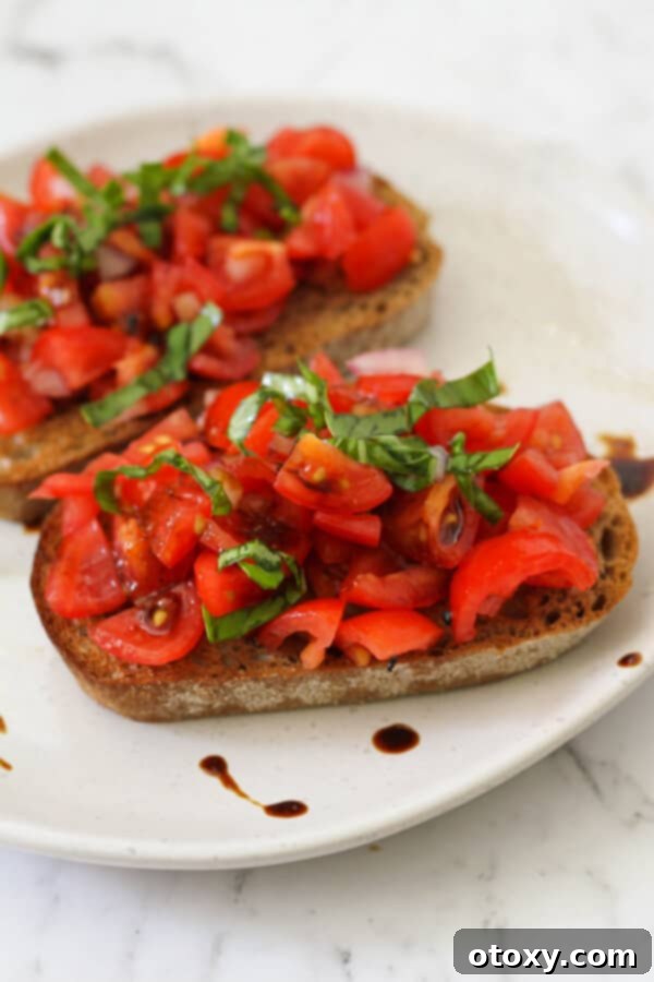 Effortless Bruschetta 2 Two pieces of classic tomato bruschetta with balsamic glaze on a white plate, showcasing fresh ingredients and a beautiful presentation.