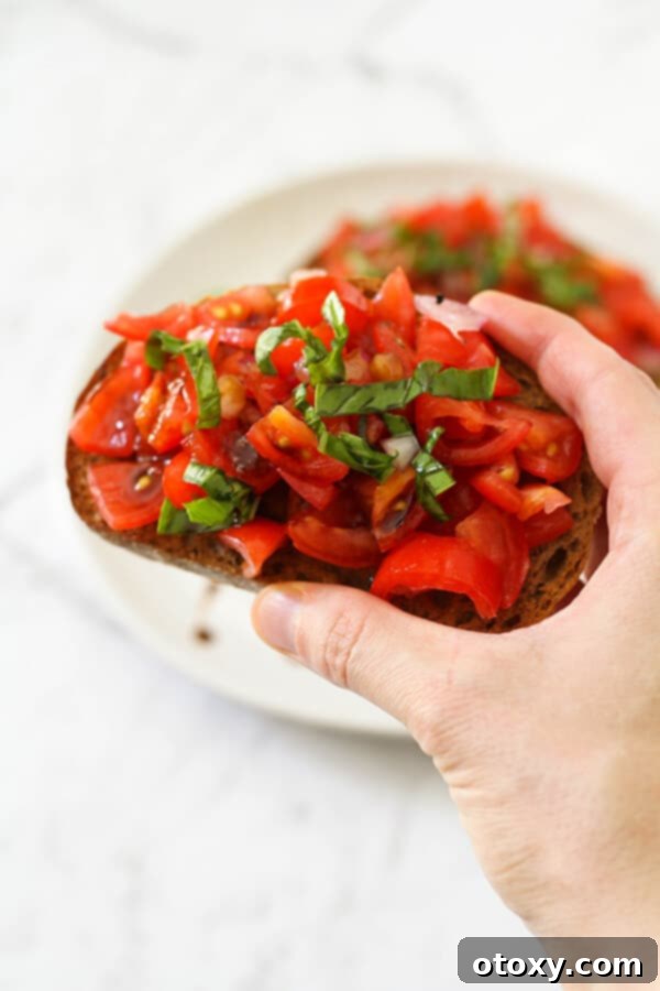 Effortless Bruschetta 4 A hand holding a single piece of freshly made bruschetta, highlighting its vibrant toppings and perfect toast.
