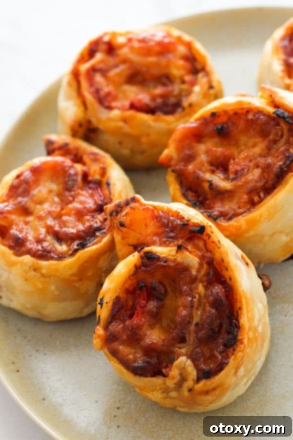 Close-up of golden pizza pinwheels on a rustic grey plate, showcasing their spiraled layers and melted cheese.