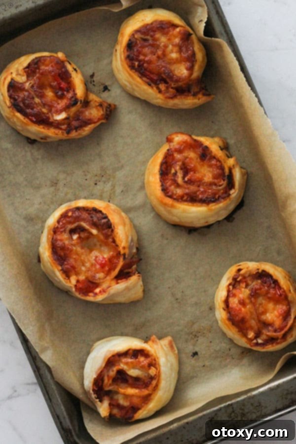 Golden-brown pizza pinwheels baking in the oven on a tray lined with parchment paper, cheese bubbling.