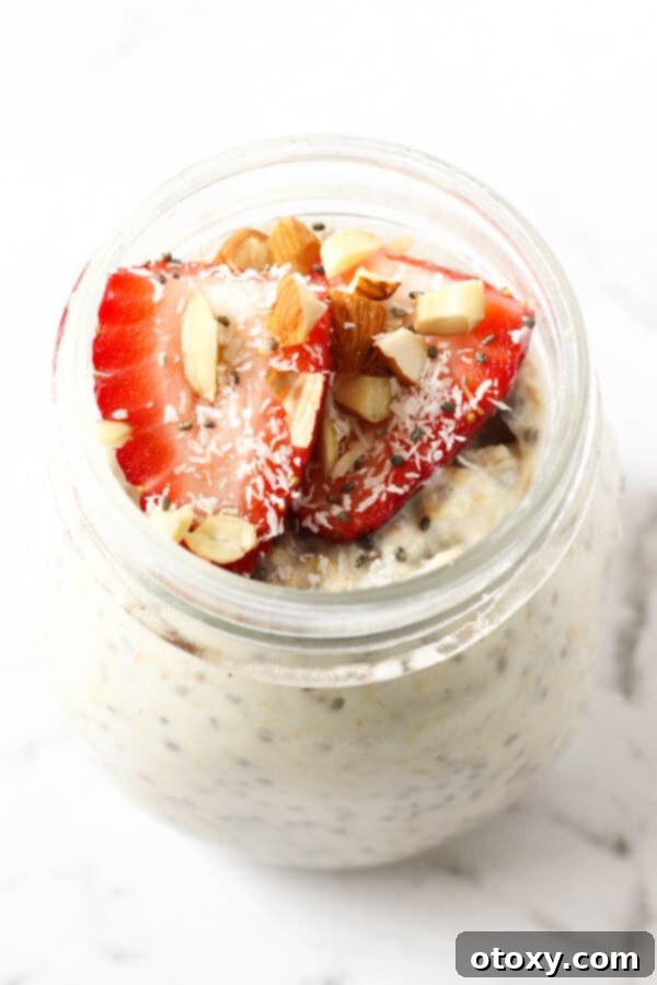 Nutritious Overnight Oats 3 Close-up of a glass jar filled with creamy overnight oats, garnished with ripe strawberries, toasted coconut flakes, and crunchy almond slivers.