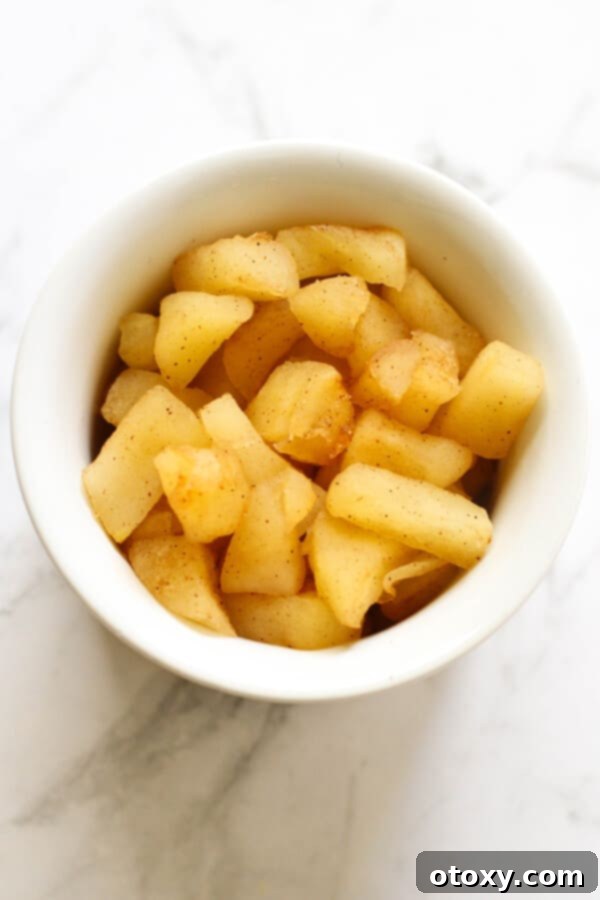 A close-up shot of tender stewed cinnamon apple pieces glistening in a pristine white bowl, showcasing their inviting texture and rich color.
