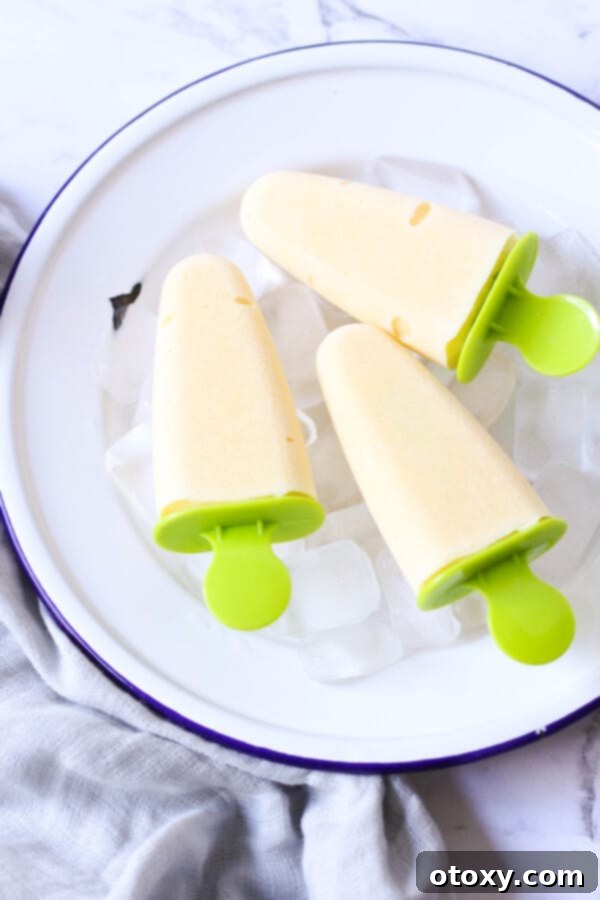 Three healthy mango popsicles garnished with fresh mint leaves, presented on a bed of ice cubes for a refreshing summer treat.