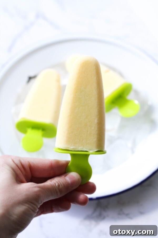 A hand holding a perfectly frozen mango popsicle against a bright, summery background, highlighting its vibrant color and smooth texture.