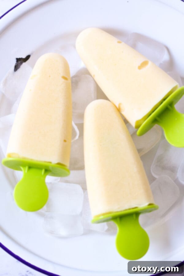 Three healthy mango popsicles garnished with fresh mint leaves, presented on a bed of ice cubes, ready for serving.