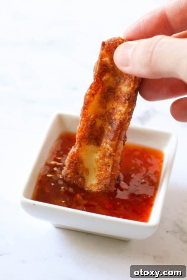 A single halloumi fry being dipped into a small bowl of sweet chili sauce, highlighting its golden texture.