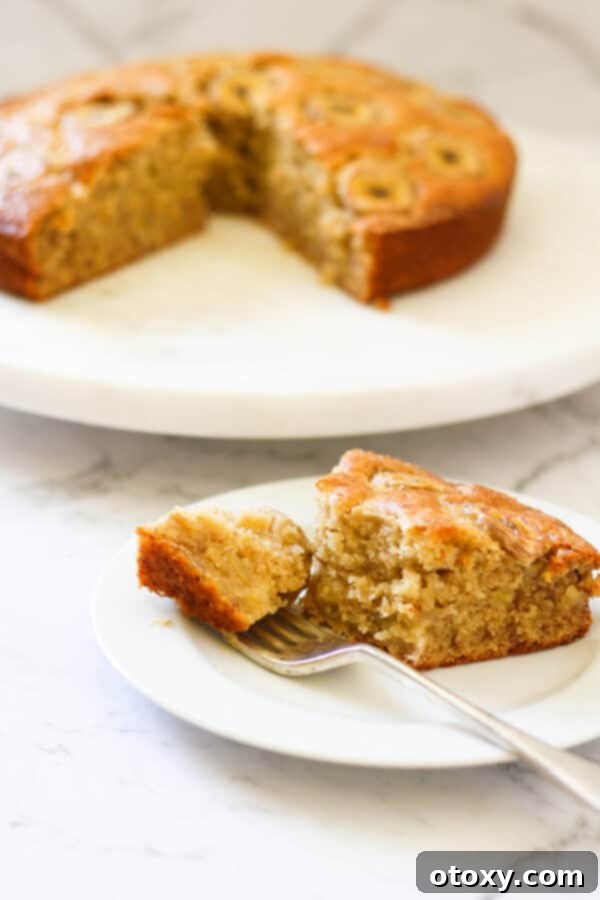 a slice of banana cake on a white plate with the rest of the cake on a wooden board behind.