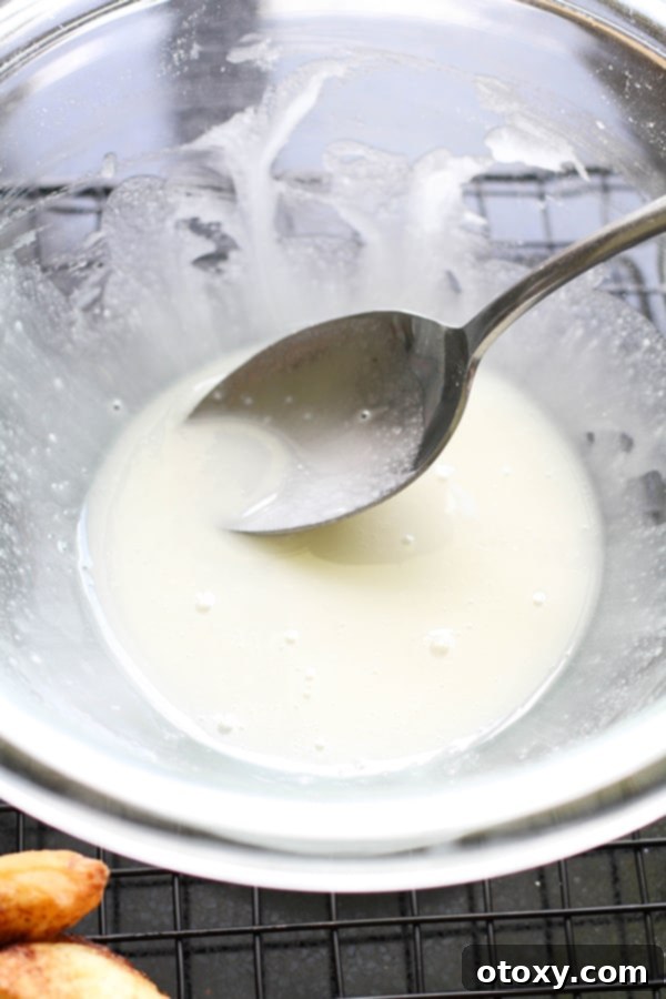 A smooth, white cinnamon roll glaze in a clear glass bowl, ready for drizzling.