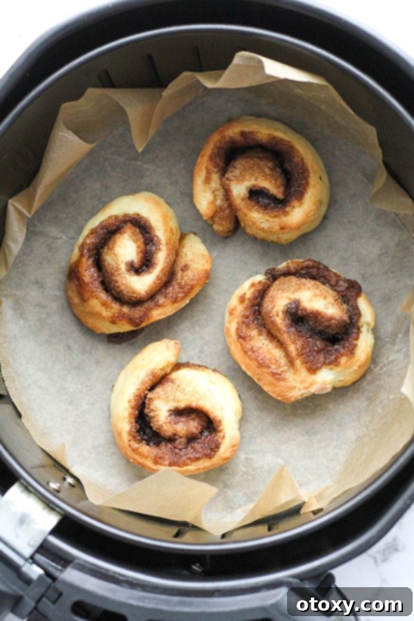 No-yeast cinnamon rolls baking to golden perfection in an air fryer basket.