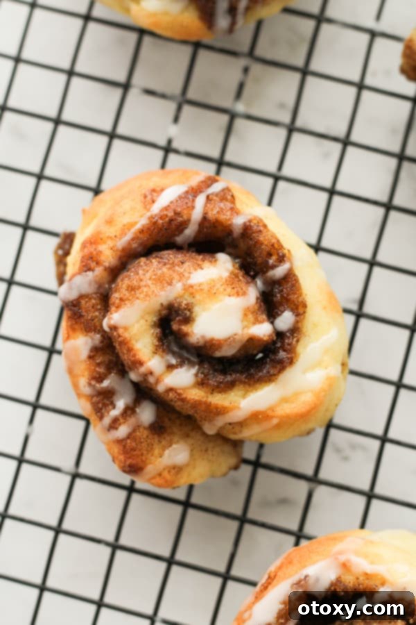 A single perfectly glazed no-yeast cinnamon roll on a wire rack, showcasing its fluffy texture.