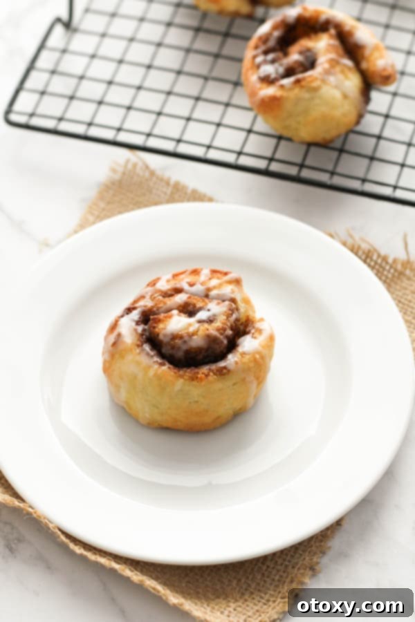 Close-up of three no-yeast cinnamon rolls on a white plate, generously covered in a sweet glaze.