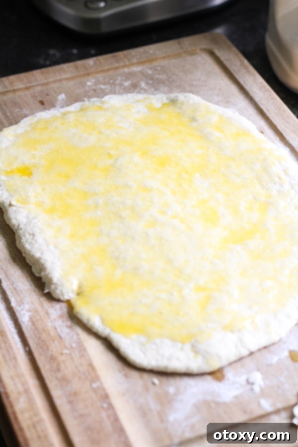 Effortless No Yeast Cinnamon Rolls Baked or Air Fried 8 Dough rolled out on a wooden board, glistening with melted butter.