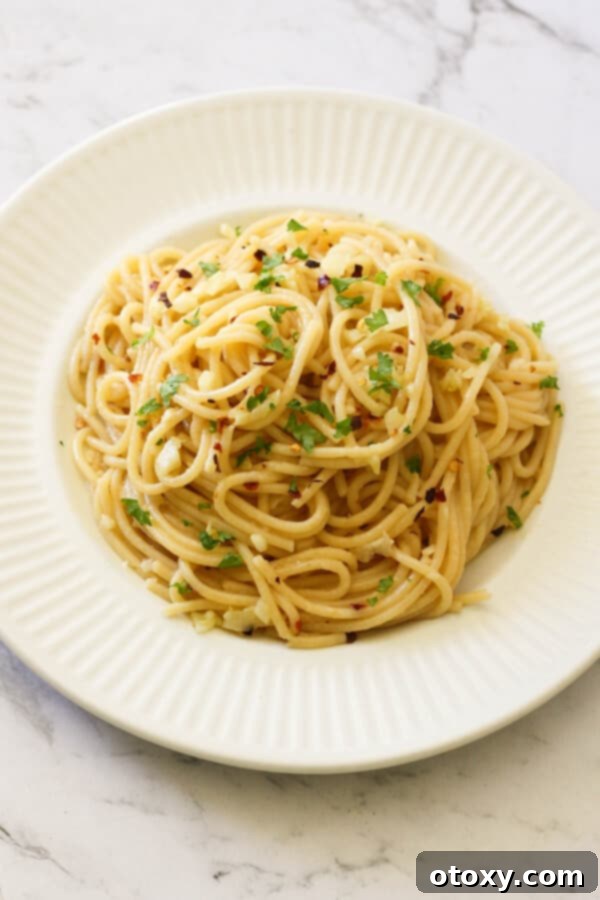 Spaghetti Aglio e Olio 3 Close-up of freshly prepared Spaghetti Aglio e Olio on a white plate, highlighting the garlic and red pepper flakes.