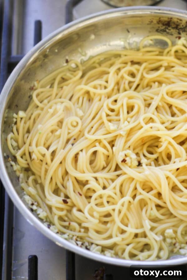 Spaghetti Aglio e Olio 7 Cooked spaghetti being tossed in a frying pan with garlic, olive oil, and a light sauce.