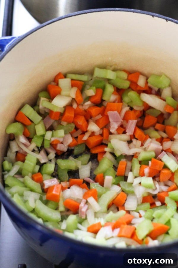 Diced onion, carrots, celery, and bacon being sautéed in olive oil in a Dutch oven, forming the essential aromatic base for Italian Minestrone Soup.