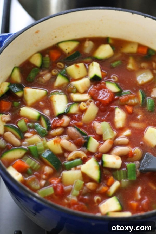 Small pasta being stirred into a large Dutch oven filled with simmering Italian Minestrone Soup, nearing the final stages of cooking.