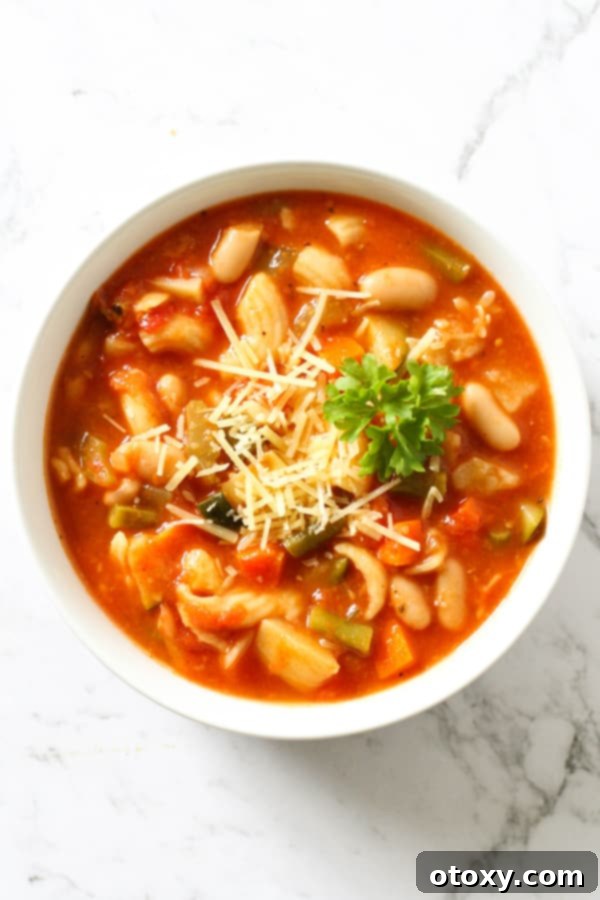 A bowl of freshly prepared Italian Minestrone Soup, artfully garnished with a sprig of fresh basil and a generous dusting of grated Parmesan cheese.
