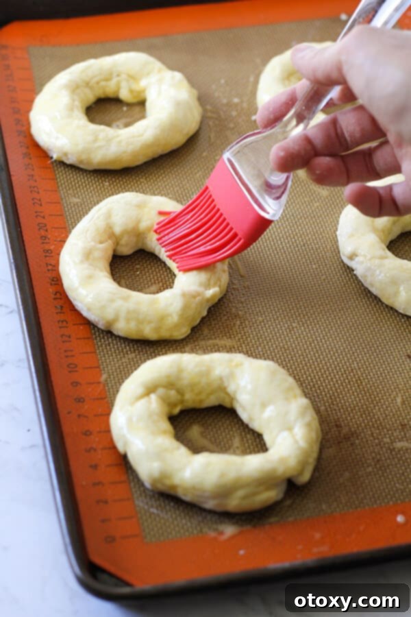 Speedy Yeast Free Bagels 8 A hand brushing an uncooked bagel with egg wash on a baking tray.