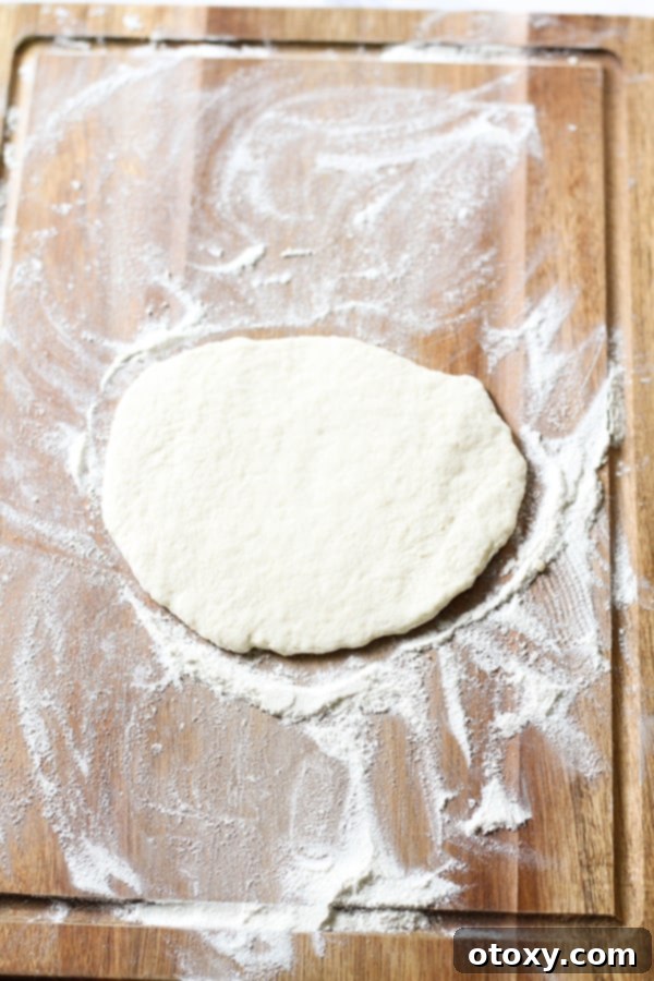 Flattened pizza dough, ready for toppings, on a wooden surface.