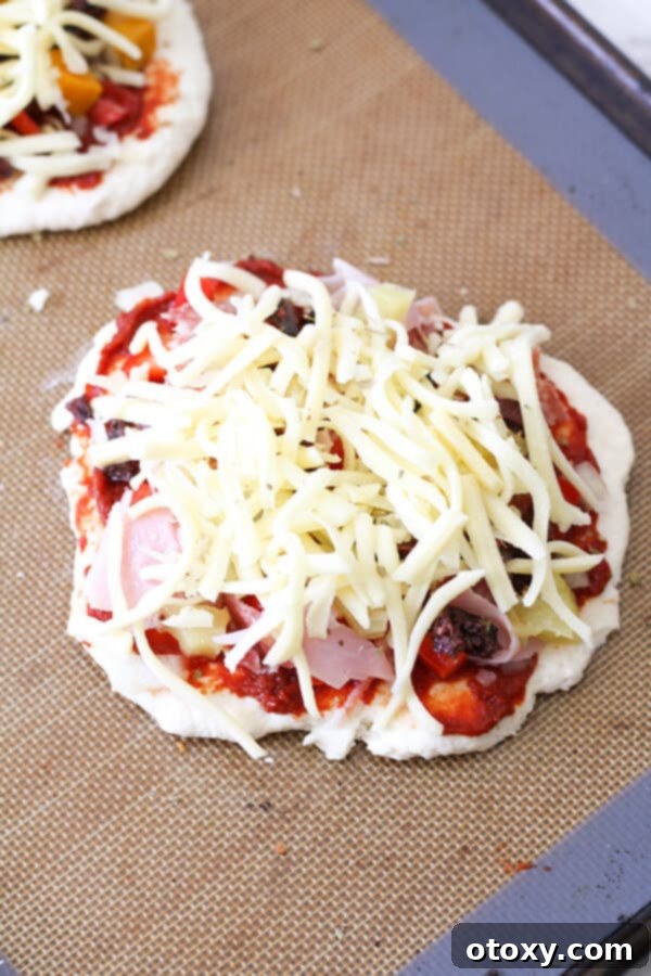 Three mini pizzas loaded with supreme toppings, ready for the oven on a baking tray.