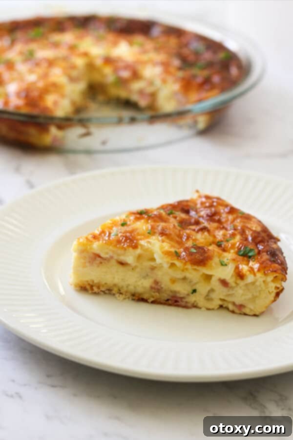 A perfectly sliced portion of fluffy Impossible Quiche resting on a pristine white plate, showcasing its rich ham and cheese fillings.