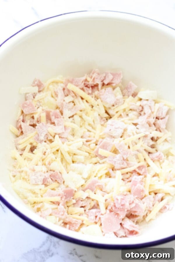 All the delicious ingredients for Impossible Quiche, including ham, cheeses, and onion, mixed together in a large bowl, ready to be transferred to the pie dish.