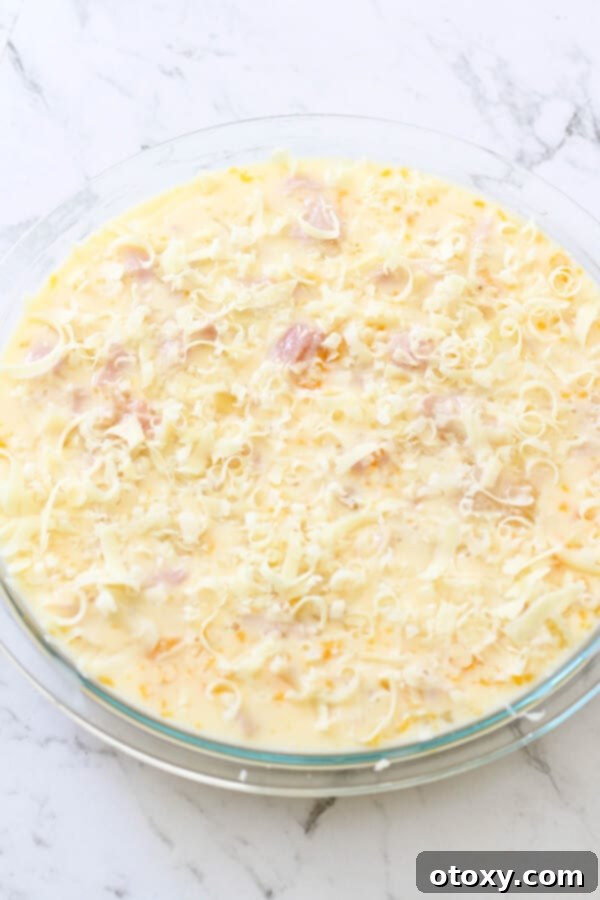 The Impossible Quiche mixture, with egg and cheese, perfectly assembled in a pie dish and poised for baking in the oven.