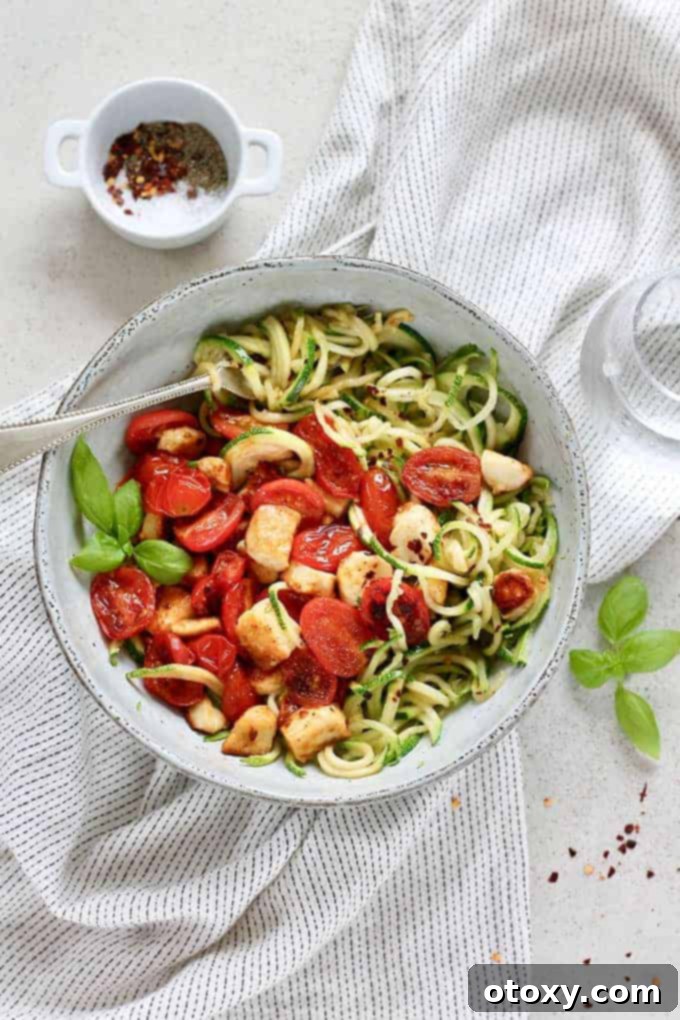A bowl of Warm Zucchini Noodle Salad with fried halloumi and burst tomatoes.