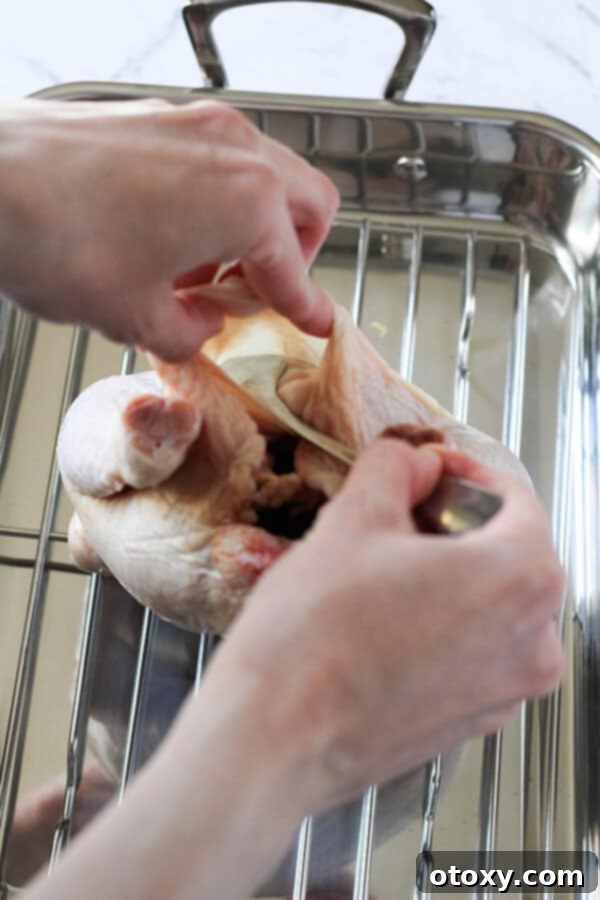 A close-up of a hand gently using a dessert spoon to separate the skin from the chicken breast, creating a pocket for the butter mixture.