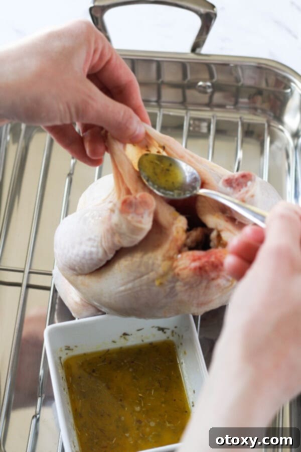 Hands carefully pouring the lemon-herb butter mixture directly under the loosened skin of a whole chicken, ensuring even distribution over the breast.