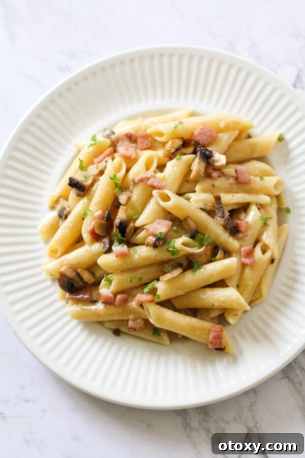Creamy Carbonara on a white plate, garnished with fresh parsley.